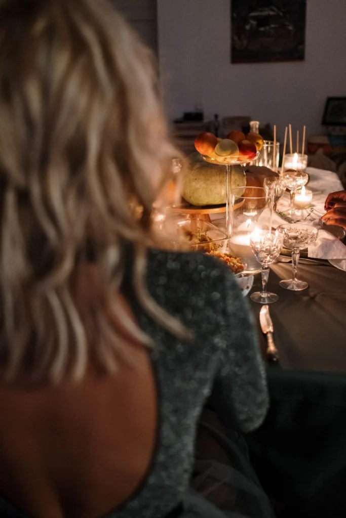Over-the-shoulder shot of woman sitting at Thanksgiving table - pin image for plus size thanksgiving outfits post