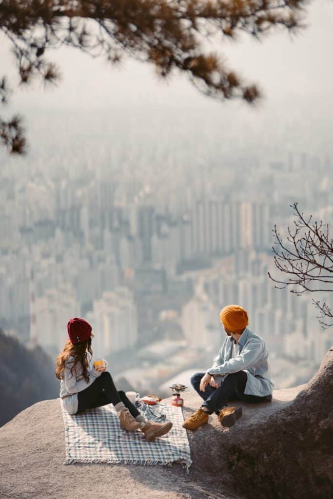 A couple overlooking a city scape during a picnic. Pin image for 41 adventure ideas for couples post.