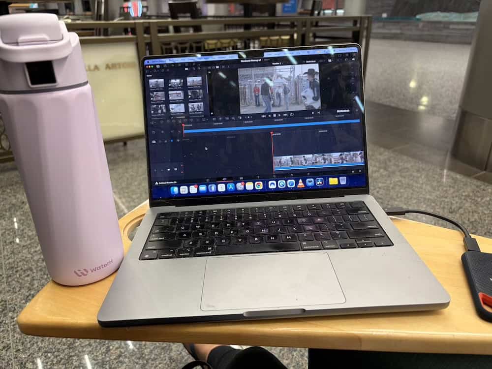 A purple WaterH water bottle sitting on a table next to a MacBook Pro with Davinci Resolve open on the screen. Editing on a film in the airport.