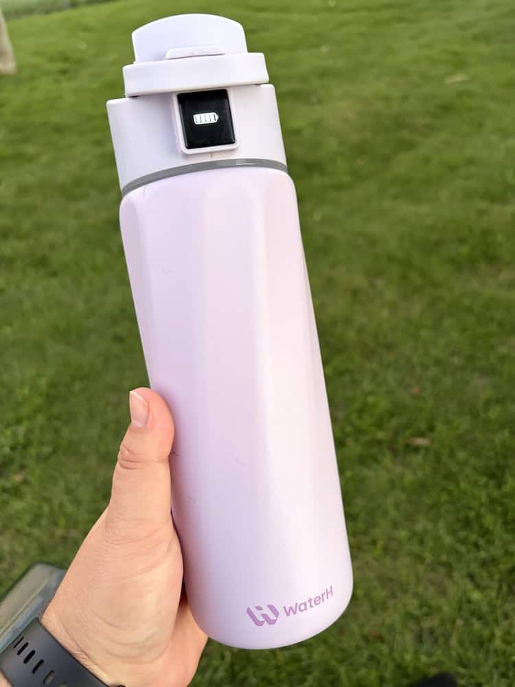 A purple WaterH smart bottle with a battery symbol lit up on the screen.
