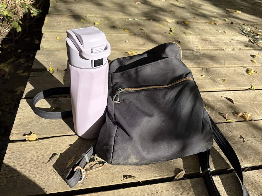 A purple WaterH smart bottle sitting next to a black Travelon convertible backpack.